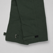 Close-up of spruce green trousers showing the hem with adjustable hook-and-loop strap closures on a light gray background.