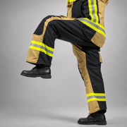 Side view of a firefighter lifting one knee while wearing gold-and-black RDG60 turnout pants.