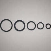 Five black circular rubber gaskets or seals of varying sizes arranged in descending size order against a plain light gray background.
