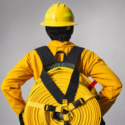 Firefighter wearing a loaded Strike Team Fireline Hose Pack with coiled yellow wildland hose and color-coded securing straps.