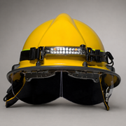 A yellow firefighter helmet with an integrated LED headlamp and a large black face shield visor, photographed against a neutral gray studio background.