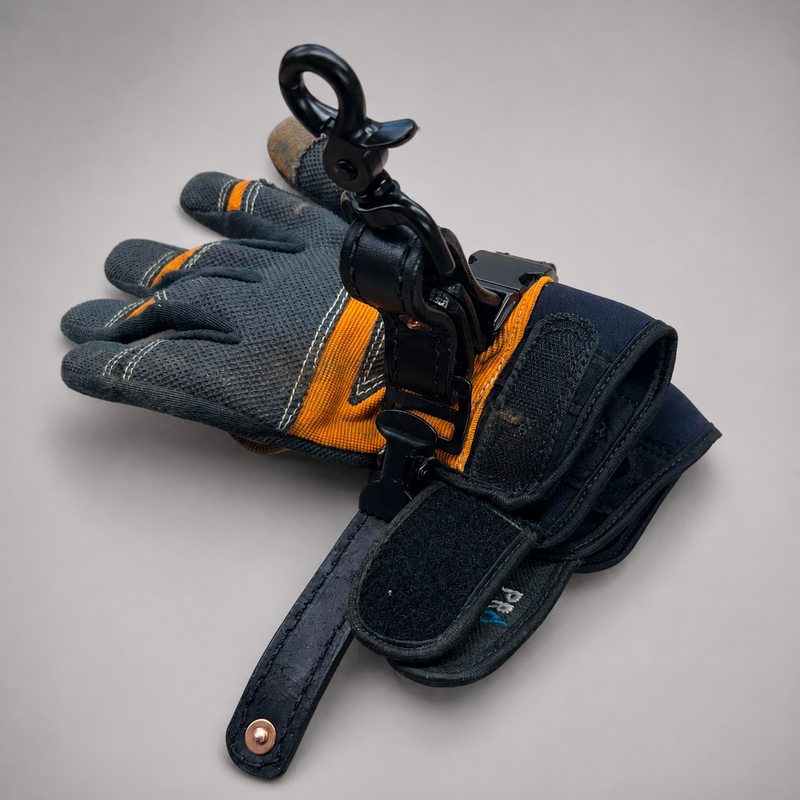 A pair of dark gray and orange work gloves with a black metal swivel hook and wrist strap attached, photographed on a neutral light gray background.