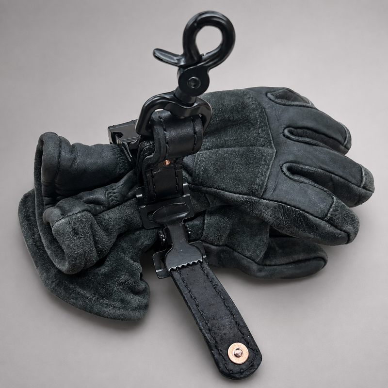 A pair of black leather and suede gloves with a black metal snap hook and strap accessory, displayed on a neutral gray background.