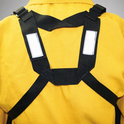 A close-up of a black webbed harness or strap system worn over a bright yellow garment, showing reflective white rectangular patches on the shoulder straps.