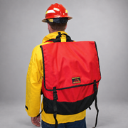Firefighter wearing the red Strike Team Phoenix Hose Pack, showing the protective flap, quick-release buckles and reinforced black base.
