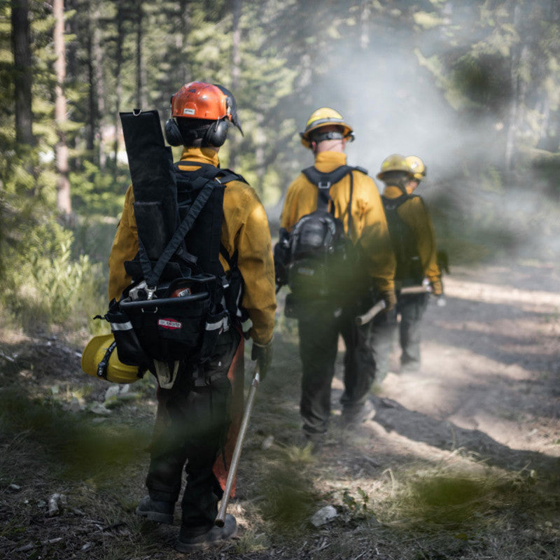 Wildland sawyer wearing a True North Chainsaw Pack while walking with a fire crew on a smoky forest trail