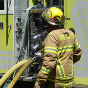 Firefighter connecting a hose to the pump panel on a yellow fire engine during operations.