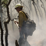 Wildland firefighter carrying a long-handled fireline tool in a smoky forest