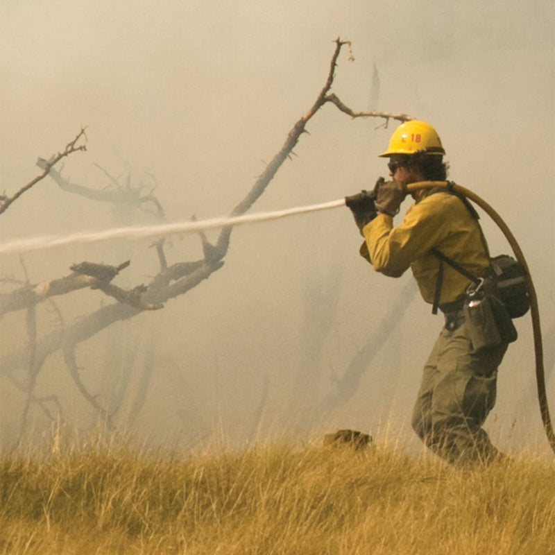Close-up of a straight-stream nozzle directing water onto a burned wildland area