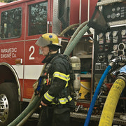 Firefighter beside a fire apparatus pump panel with pressure and intake gauges
