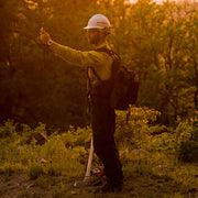 Person wearing a hard hat holding a handheld meter at arm’s length outdoors
