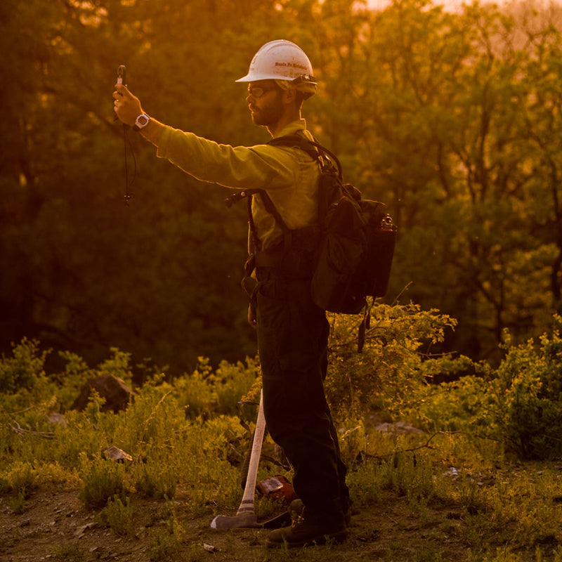 Person wearing a hard hat holding a handheld meter at arm’s length outdoors