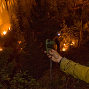 Hand holding a weather meter with burning vegetation in the background
