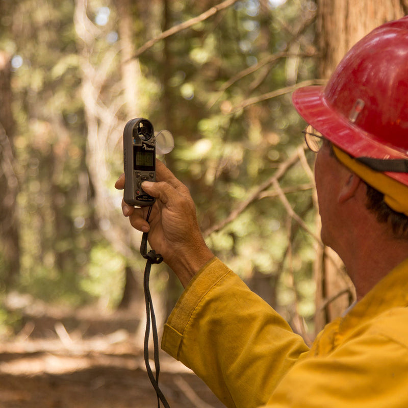 Firefighter holding a Kestrel weather meter in a wooded area