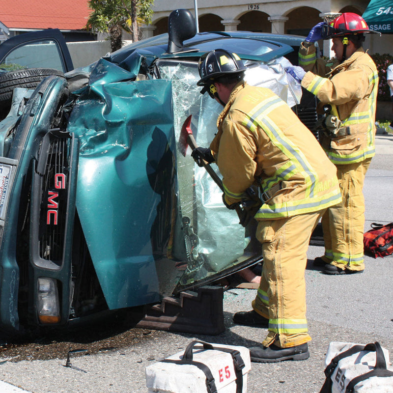 Firefighter using a pick head axe on the windshield of an overturned vehicle during extrication.