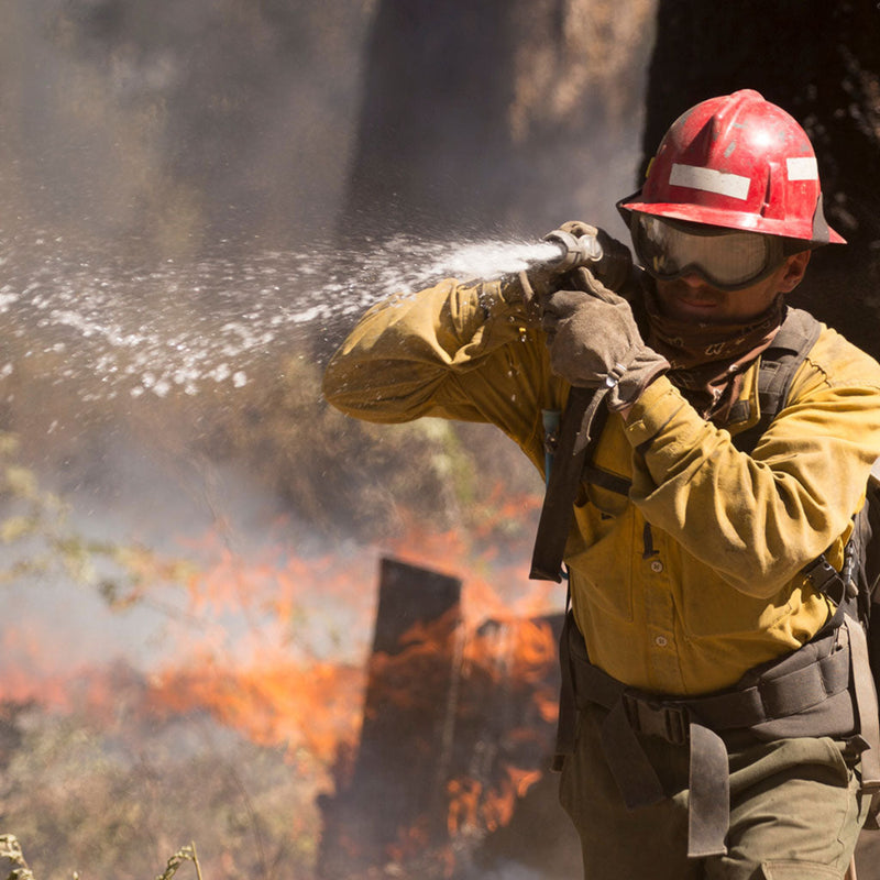 Wildland firefighter operating an S&H Twin Tip Forestry Nozzle near active flames