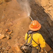 Wildland firefighter using a small hose to spray a smoldering log