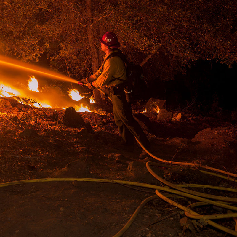 Wildland firefighter operating a hose line during active fire suppression