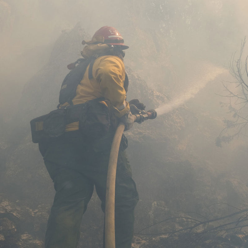 ildland firefighter directing a fire hose stream through heavy smoke