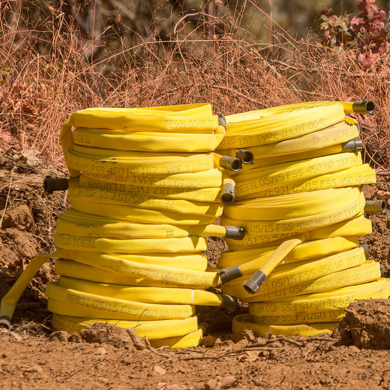 Coiled yellow forestry fire hose with aluminum couplings staged outdoors